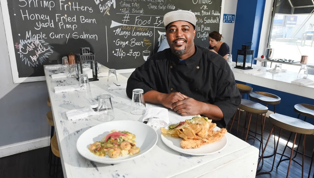 Chef Max Hardy in his restaurant kitchen with two plated shrimp dishes