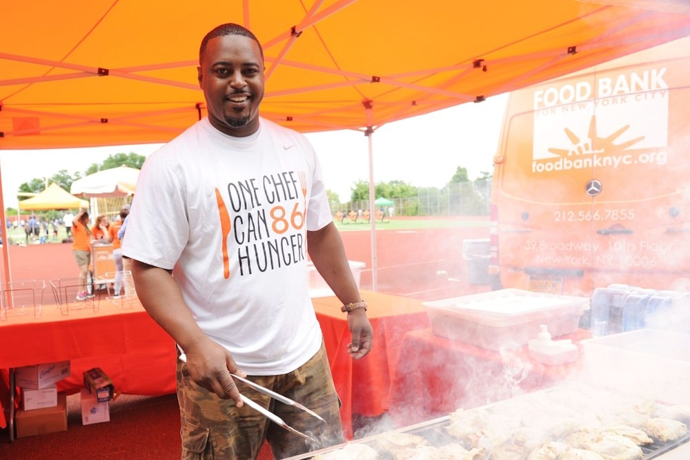 Chef Max Hardy grilling at a Food Bank event in a One Chef Can 86 Hunger shirt