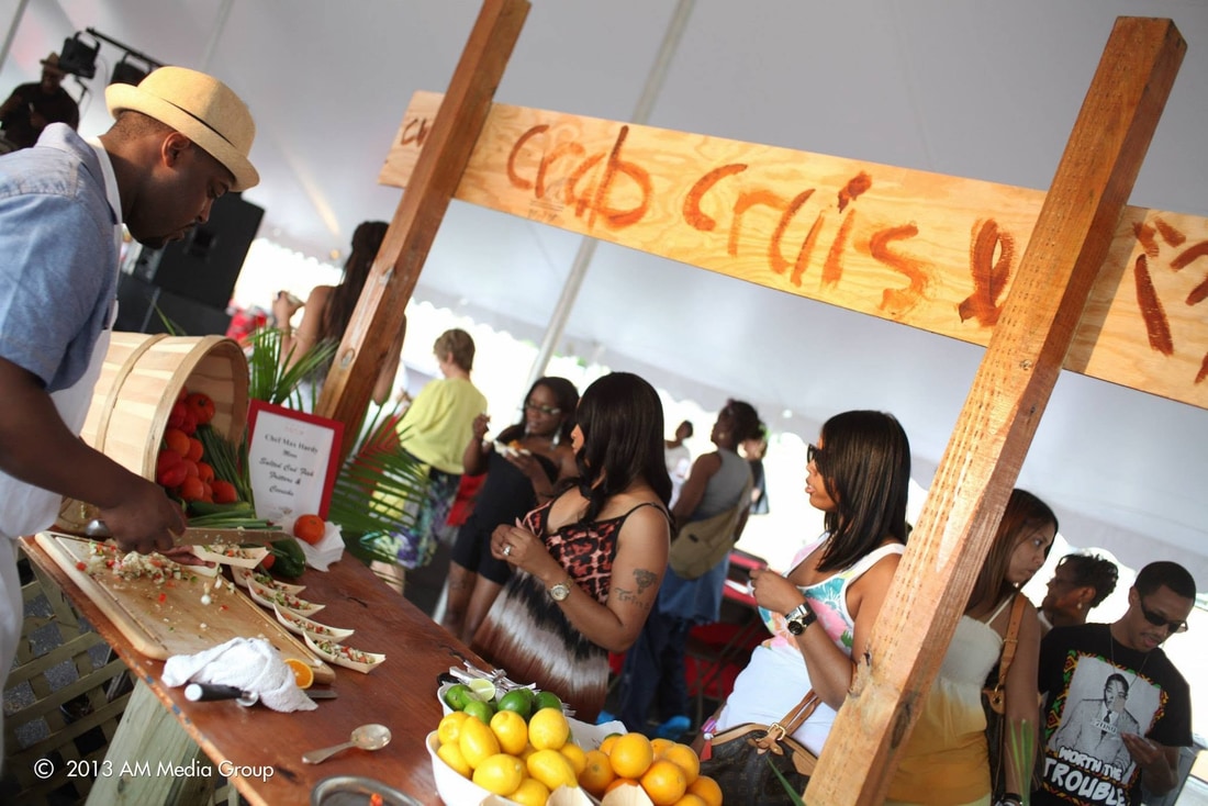 Chef Max Hardy preparing seafood at his chef table under the tent with guests watching and a hand painted Crab Cruise sign