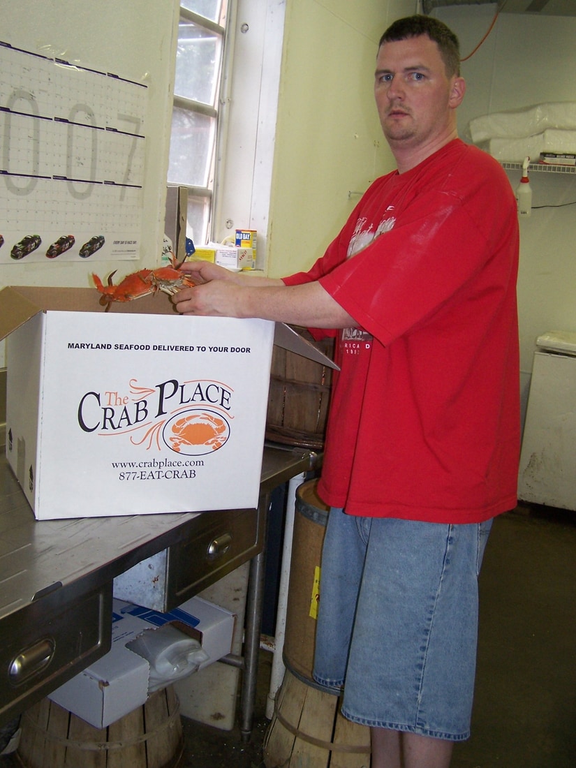 Matt, a Crab Place team member, holding a steamed Maryland blue crab over a branded Crab Place shipping box in 2007.