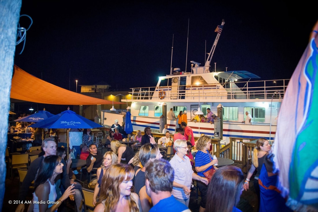 Nighttime crowd on the dock at Treasure Island beside a lit boat
