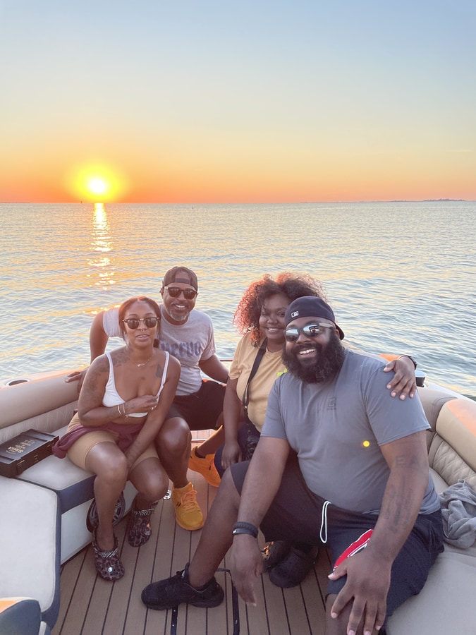 Four friends on a pontoon boat at sunset over calm bay water