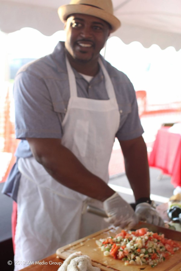 Chef Max Hardy in a straw hat and apron cutting seafood ceviche on a board at the event tent
