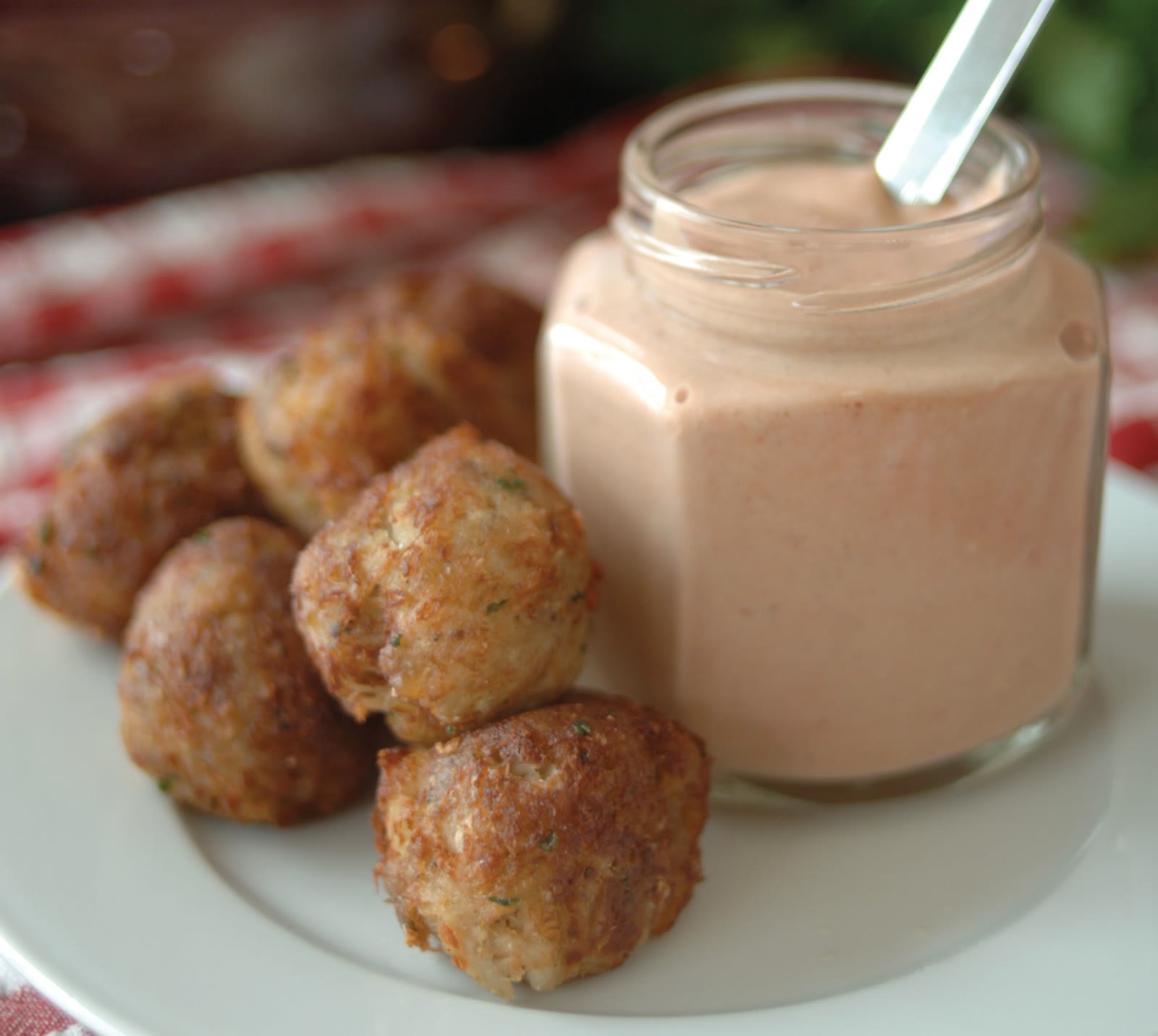Six golden fried 2 oz Maryland crab balls on a white plate beside a glass jar of pink dipping sauce.