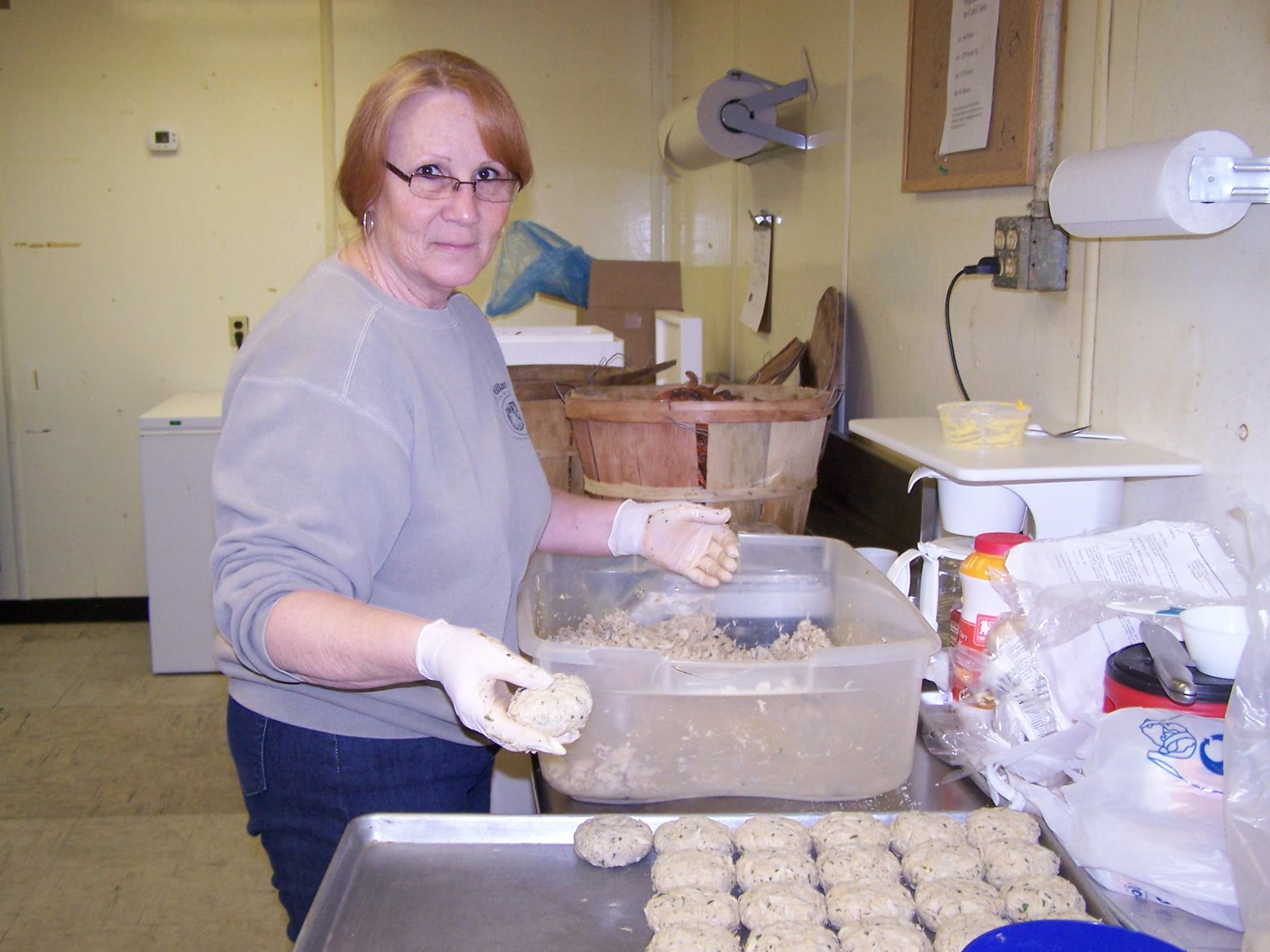 A photo from about 15 years ago of a Crab Place employee in gloves forming crab cakes by hand at a prep table, with a tray of finished cakes in front of her.