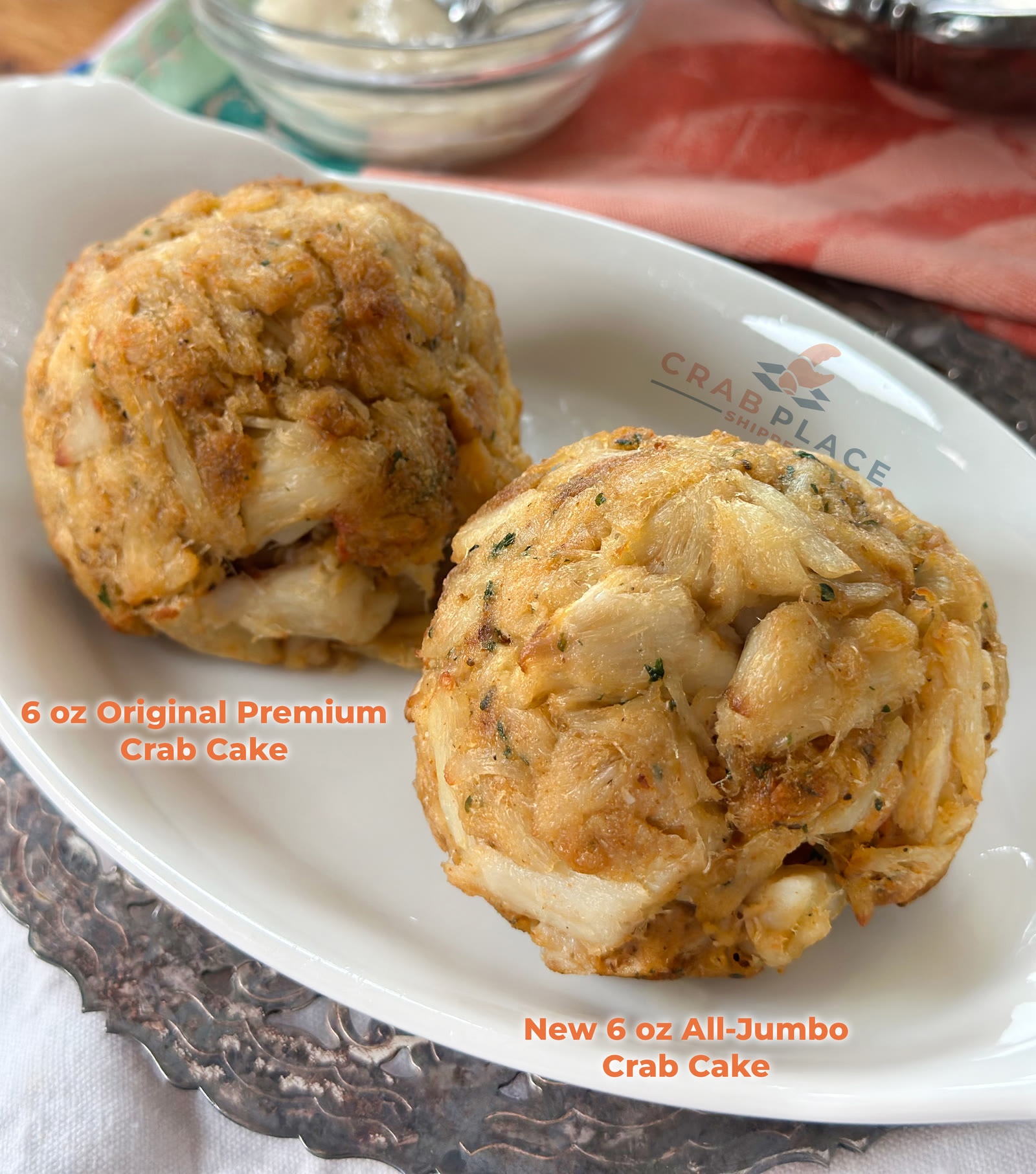 Two cooked 6 oz crab cakes side by side on a white Crab Place plate, labeled Original Premium Crab Cake and All-Jumbo Crab Cake, showing the difference in lump size.