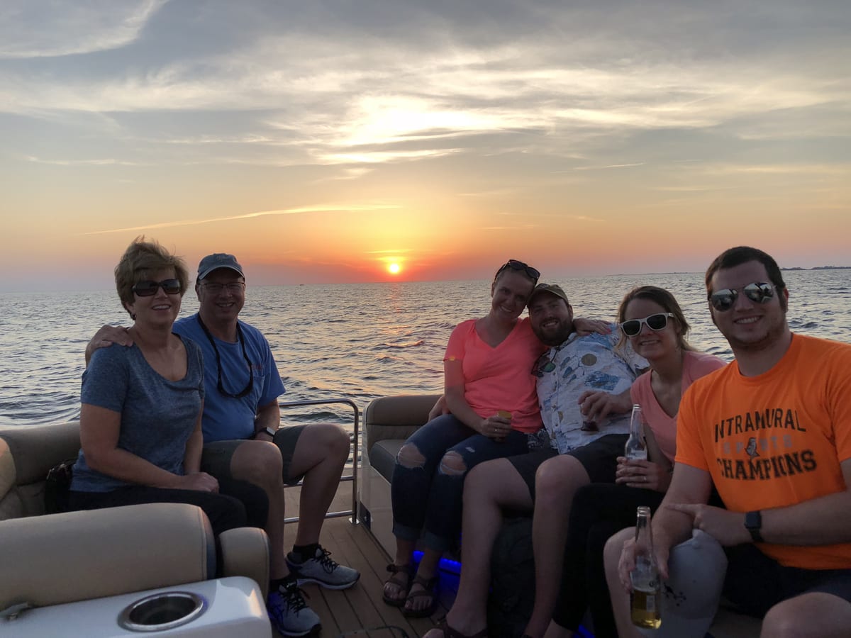 Jeff Klingeman and his family sitting together on a pontoon boat at sunset on the water off Crisfield, Maryland, with the sun low over calm water behind them.