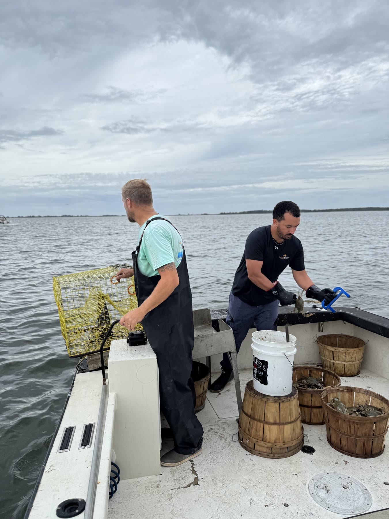 Two watermen unloading bushel baskets of live crabs from a boat at the dock