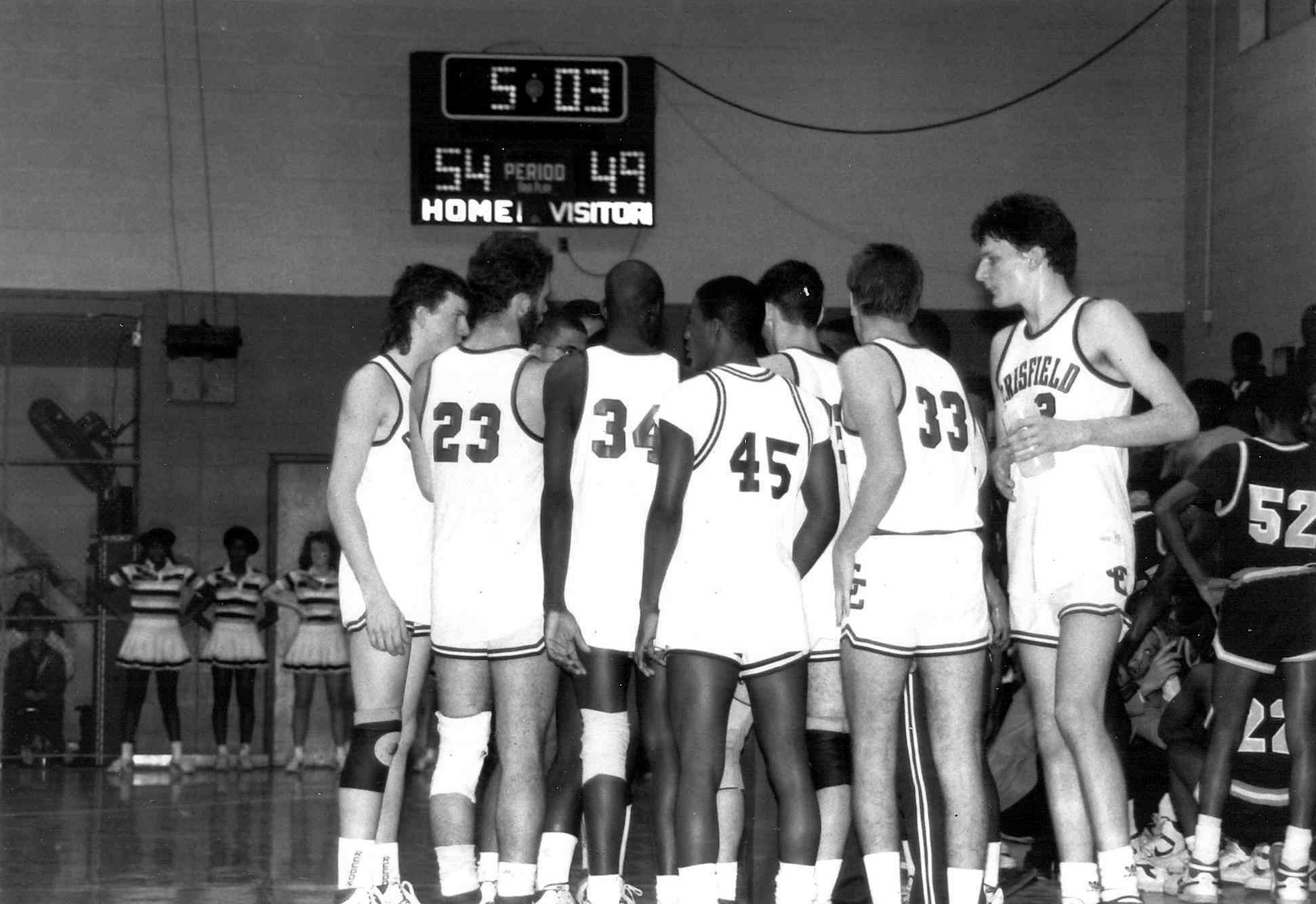 Black and white photo of the Crisfield High basketball team huddled on the court under the scoreboard, home 54, visitor 49.