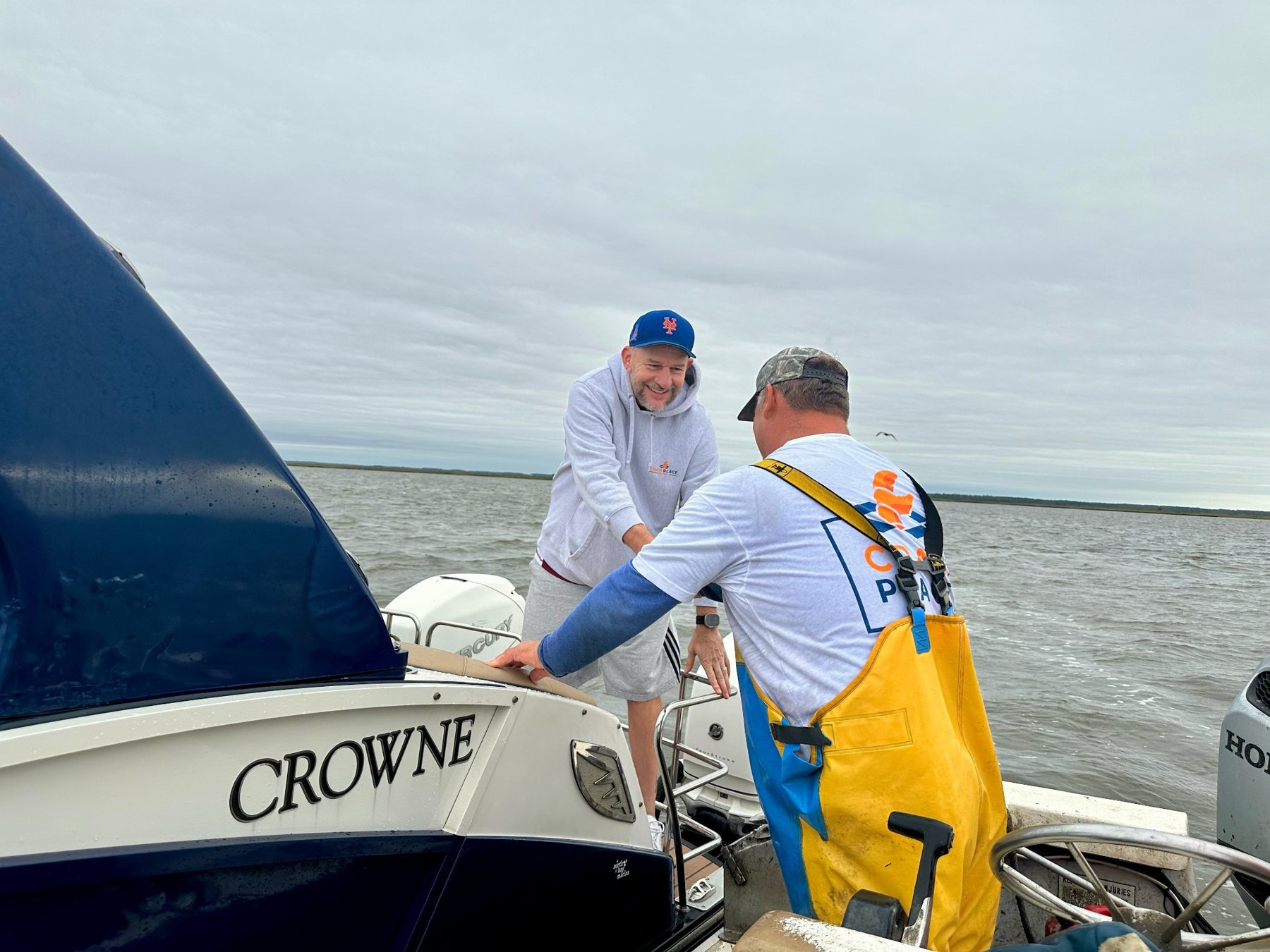 Greg Cain on a pontoon boat shaking hands with Moose Labo, who is standing on his workboat alongside.