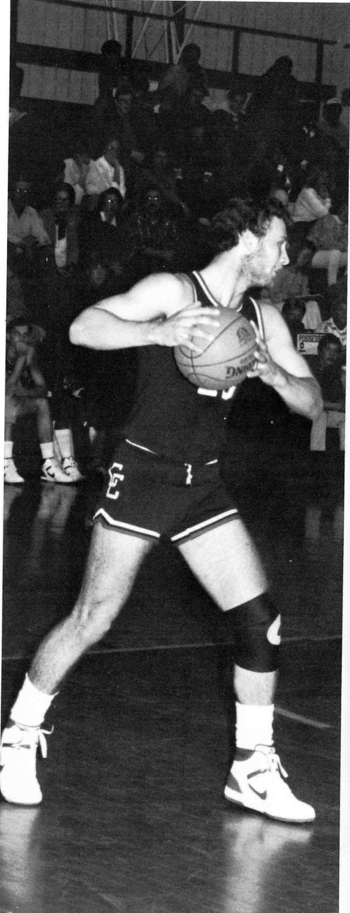 Yearbook photo of Moose Labo in a dark Crisfield uniform gripping the basketball with both hands in front of a packed gym.