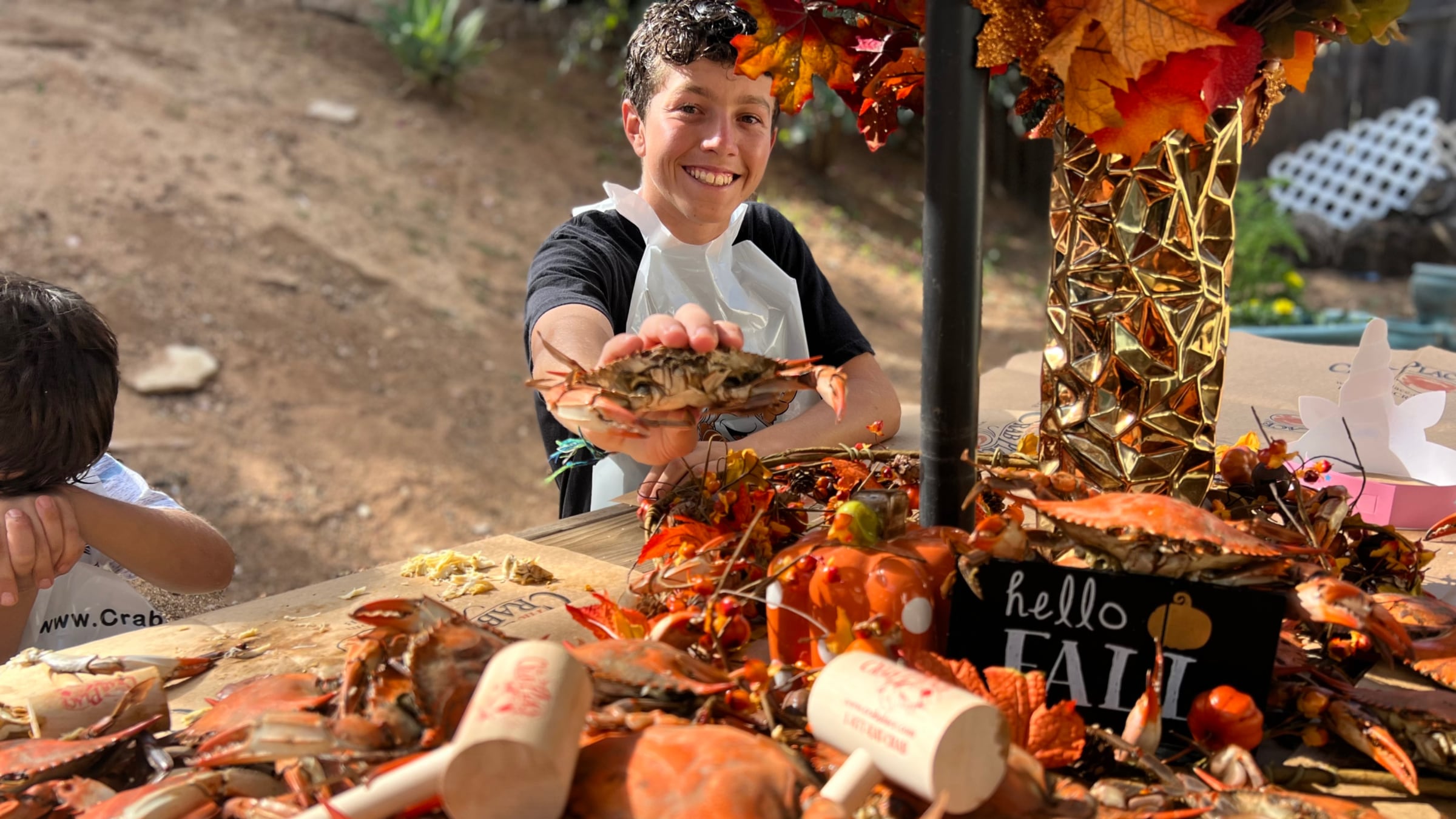 A customer holding up a steamed crab at his family's fall crab feast, the table covered in Crab Place paper, pumpkins and autumn leaves