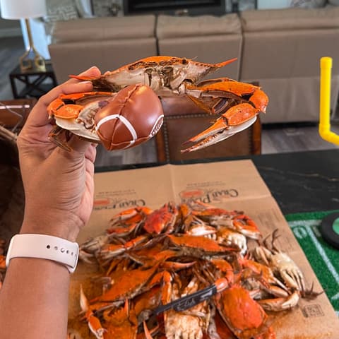 A hand holding up a steamed crab painted like a football over a pile of crabs