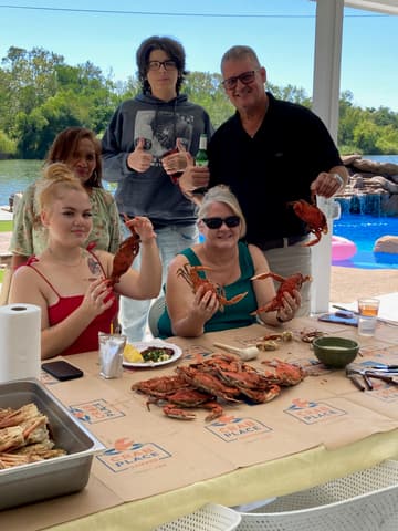 A family holding up crabs at a poolside table