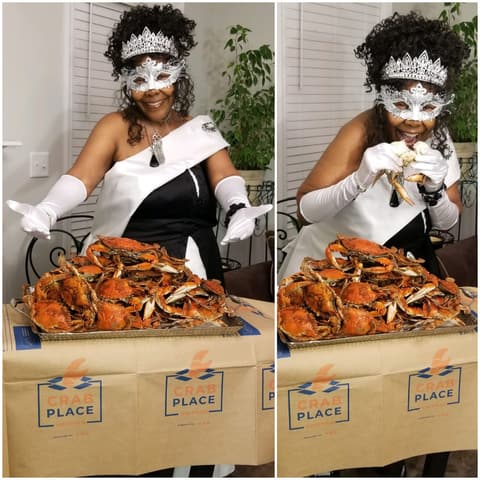A customer in a masquerade mask and gloves posing with a tray of steamed crabs