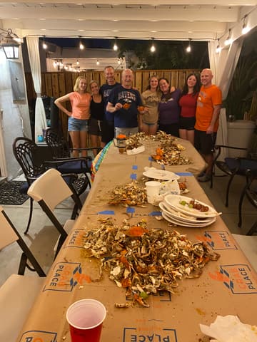 A group of friends at the end of a long patio table covered in crab paper and shells