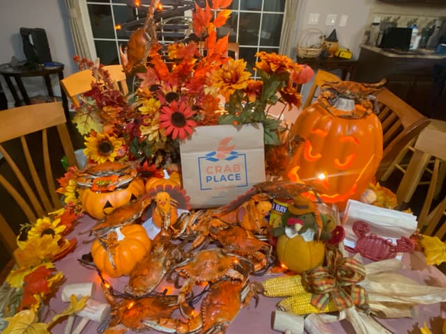 A table piled with crabs, a carved pumpkin, sunflowers and fall leaves around a Crab Place box