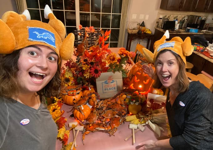 Two customers in turkey hats laughing behind a table of crabs, pumpkins and fall leaves