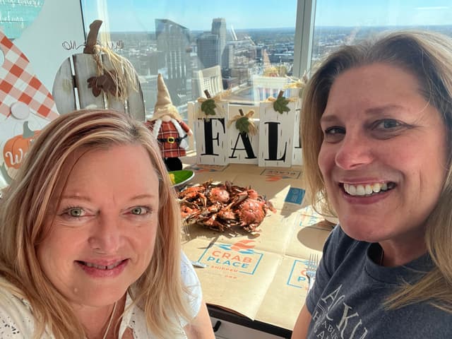 Two customers taking a selfie with their fall crab feast in a high rise with the city behind them