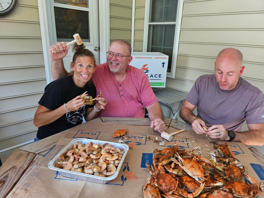 Three friends on a porch cracking steamed crabs with a tray of shrimp