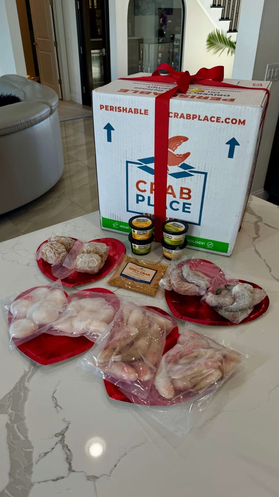 Scallops, shrimp, crab claws and crab cakes laid out on heart plates in front of a Crab Place box